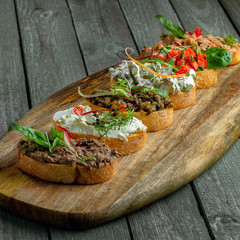 Bruschetta set made of tomato, meat pate, olives, cream cheese and tuna salad on a rustic wooden...