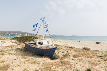 Fototapeta na wymiar Old wooden fishing boat on the beach with Greek flags on the mast. Naxos island, Greece