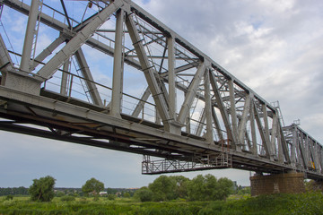 Railway bridge made of iron structures, against a cloudy sky background