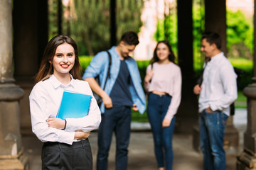 Obraz premium Beautiful young college student standing in front of her friends holding her books at campus. Education togetherness relationships friendship study campus concept