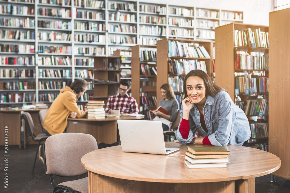 Poster portrait of glad woman working with notebook computer while leaning on table in library