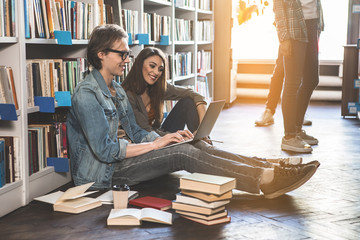 Side view optimistic male and beaming lady typing in laptop while locating on floor in athenaeum