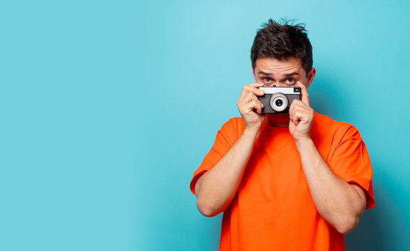 Young handsome man in orange t-shirt with vintage camera. Studio image on blue background