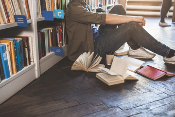 I am so tired. Male sitting on floor near different books. He drinking cup of coffee