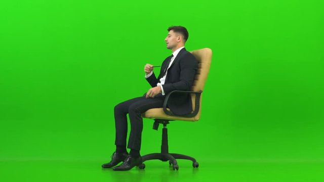 The businessman talking on the office chair on the green background