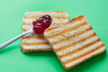 Slices of toast bread and tea spoon with jam on green background, top view