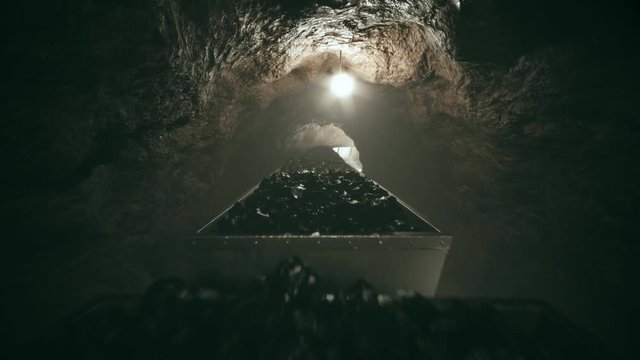 Full of coal mine wagons slowly moving through narrow underground tunnel.