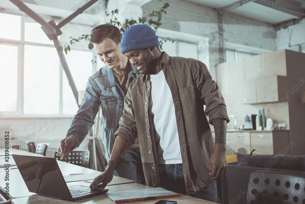 Poster attentive colleague. professional young optimistic guys are smiling while standing near table and lo