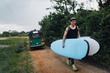 a man happily carries two surfboards from   taxi on the way