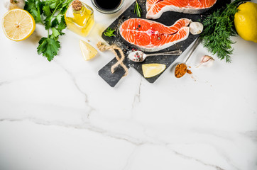 Raw salmon fish steaks with lemon, herbs, olive oil, ready for grill, slate cutting board, white marble background copy space above