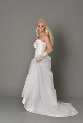 full length portrait of blonde  girl wearing white fantasy gown. standing pose in side profile, grey studio background.