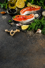 Raw salmon fish steaks with lemon, herbs, olive oil, ready for grill, slate cutting board, dark rusty background copy space