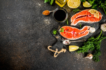 Raw salmon fish steaks with lemon, herbs, olive oil, ready for grill, slate cutting board, dark rusty background copy space