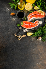 Raw salmon fish steaks with lemon, herbs, olive oil, ready for grill, slate cutting board, dark rusty background copy space