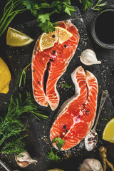 Raw salmon fish steaks with lemon, herbs, olive oil, ready for grill, slate cutting board, dark rusty background copy space
