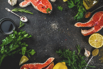 Raw salmon fish steaks with lemon, herbs, olive oil, ready for grill, slate cutting board, dark rusty background copy space