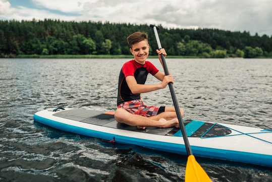 cheerful teenager sitting on a sap surf   and rowing with an oar