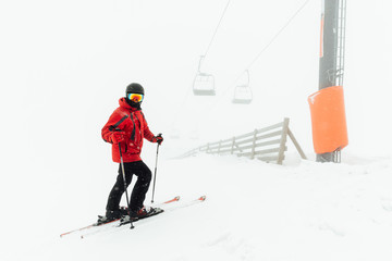 skier stands near the fence under   chair lift