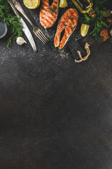 Grilled salmon fish steaks with ingredients lemon, herbs, olive oil, slate cutting board, dark rusty background copy space