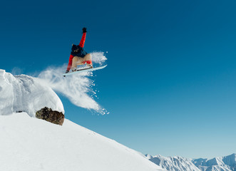   snowboarder in the outfit drops off the ledge of the stone onto the fresh snow creating a spray...