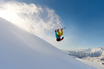 girl snowboarder jumping front flip leaving a wave of snow