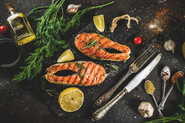 Grilled salmon fish steaks with ingredients lemon, herbs, olive oil, slate cutting board, dark rusty background copy space