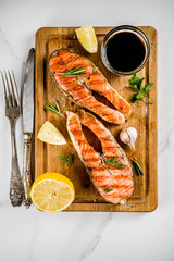 Grilled salmon fish steaks with ingredients lemon, herbs, olive oil, slate cutting board, dark rusty background copy space