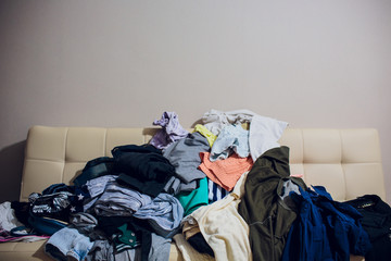 Messy clothes, lady bag and shoes scattered on leather sofa