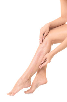Young woman applying body scrub on leg against white background