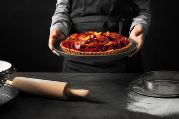 Woman holding delicious pie with plums on black background