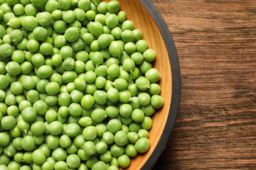 Plate with green peas on wooden background, top view