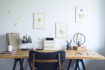 Modern home office interior with wooden desk, books,poster illustrations of plants, table lamp and office accessories. Stylish creative and vintage desk.