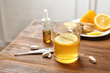 Glass with hot tea, lemon and pills for cold on wooden table