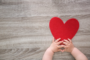 Little child's hands near red heart on wooden background, top view