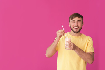 Young man with glass of delicious milk shake on color background