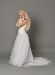 full length portrait of blonde  girl wearing white fantasy gown. standing pose in side profile, grey studio background.