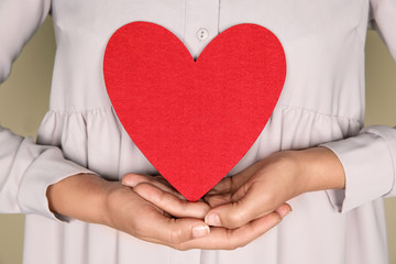 Young woman holding red heart on color background, closeup