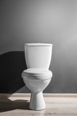 New ceramic toilet bowl near grey wall, side light