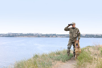 Man in military uniform with German shepherd dog near river