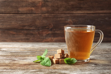 Cup with hot aromatic mint tea, fresh leaves and sugar cubes on wooden table
