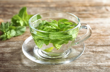 Cup with hot aromatic mint tea on wooden table
