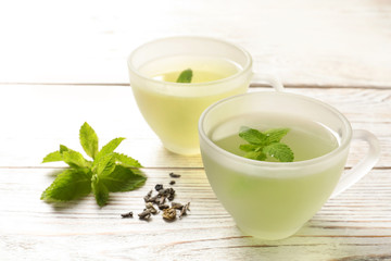 Cups with hot aromatic mint tea, fresh and dry leaves on wooden table