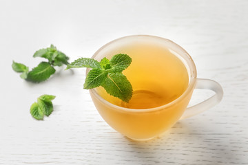Cup with hot aromatic mint tea and fresh leaves on table