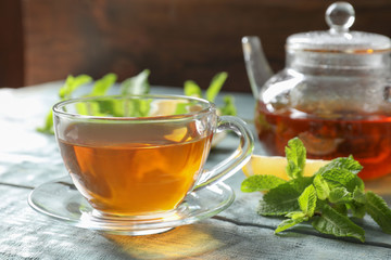Cup with hot aromatic mint tea and fresh leaves on table