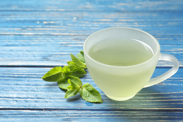 Cup with hot aromatic mint tea and fresh leaves on wooden table