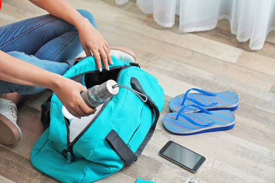 Young woman packing sports bag on floor