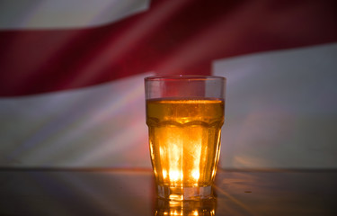 Creative concept. Pint of fresh beer on grass with blurred flag of England on background or Glass of lager beer ready for drink. Copy space.