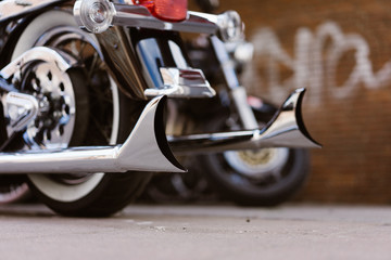 Shiny chromed retro fishtail exhausted pipes of luxury motorcycle. Brick wall with defocused...