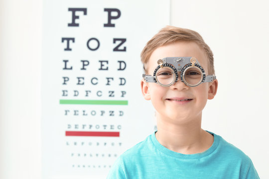 Little boy with trial frame near eye chart in ophthalmologist office