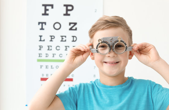 Little boy with trial frame near eye chart in ophthalmologist office